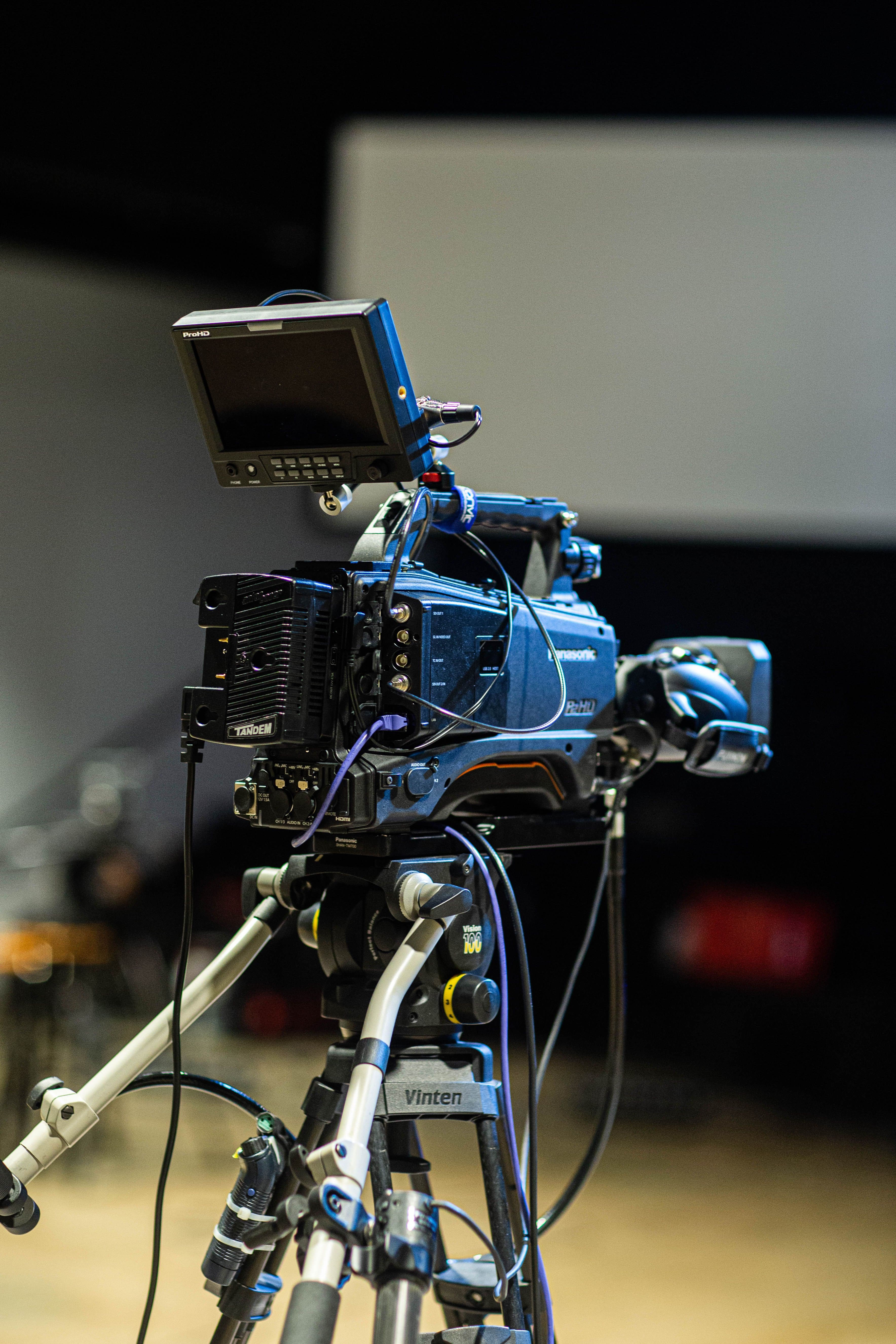 Professional broadcast camera on a tripod pointed at an event stage